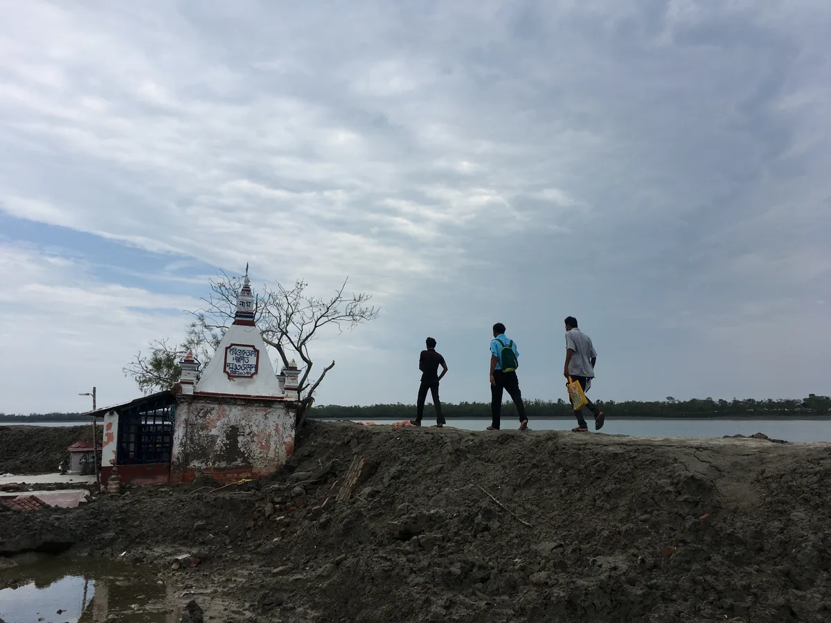 People visiting an area affected by Cyclone Amphan with a temple partly submerged in mud