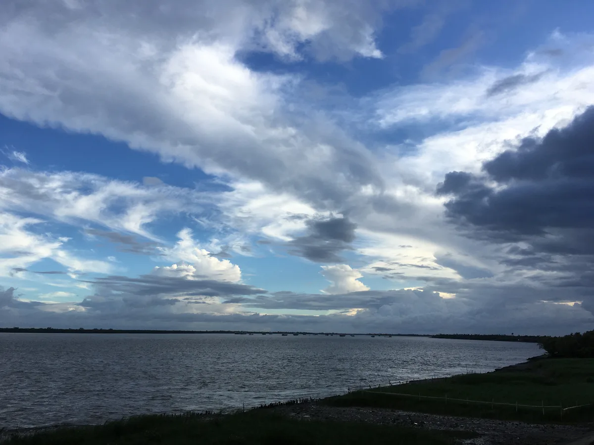 Riverbank beneath a crescent-shaped moon and cloudy sky