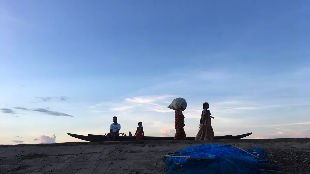 People walking along a river embankment with a boat nearby