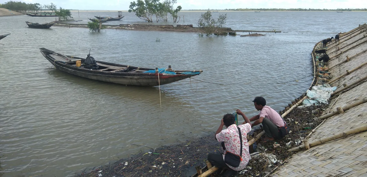 Two men planting mangrove saplings beside a river