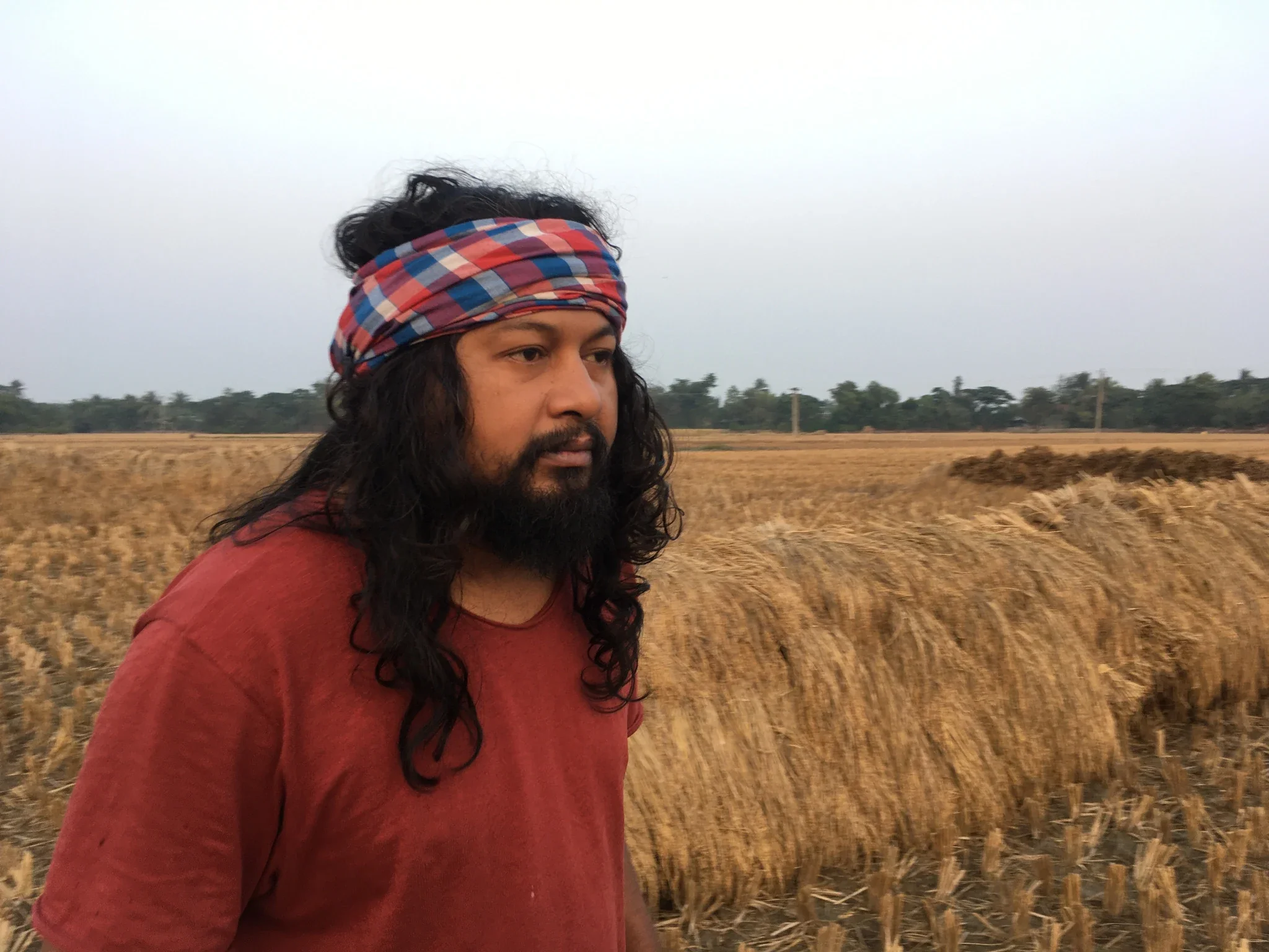 Saurav Moni standing in a rural agricultural landscape of Bengal